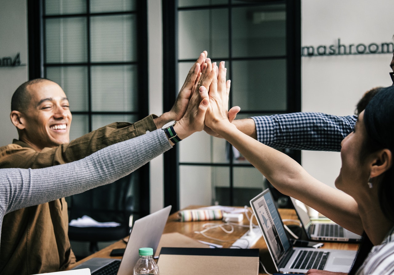 Excited multiethnic work team give high five motivated for shared success at office meeting.